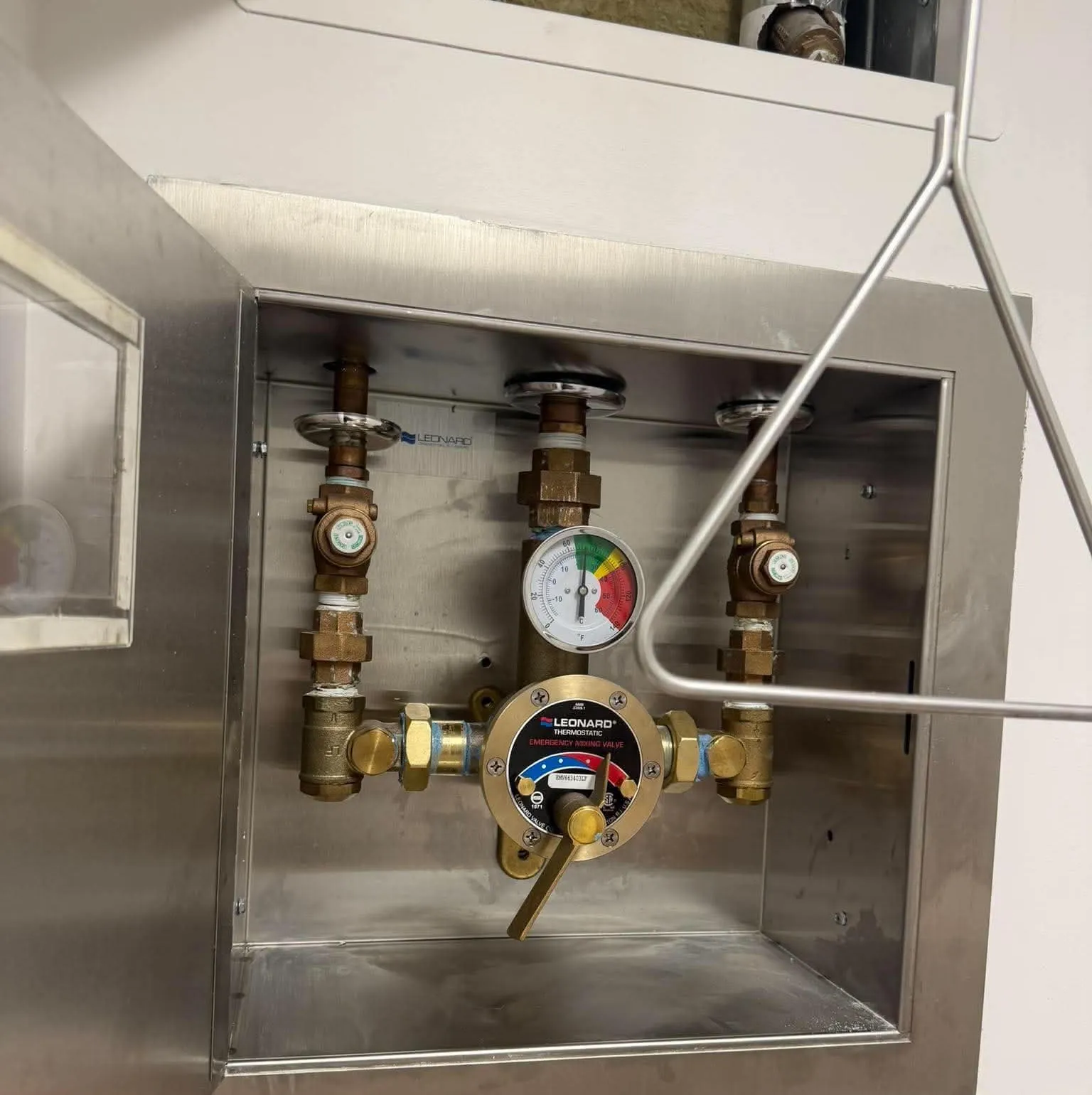 Mitigeur thermostatique d’urgence en laiton dans un cabinet d’acier inoxydable, thermomètre dans le vert, à côté de la poignée de la douche d’urgence